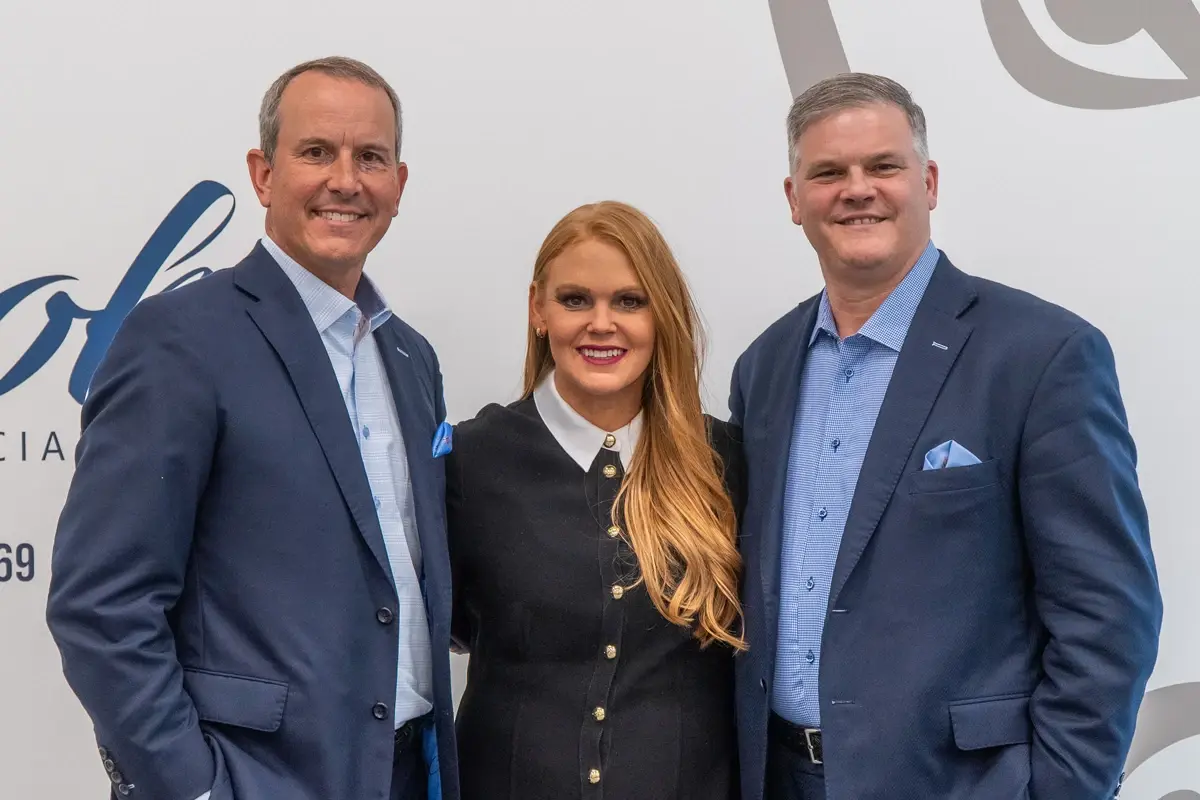 Three wealth advisors smiling in front of a logo wall
